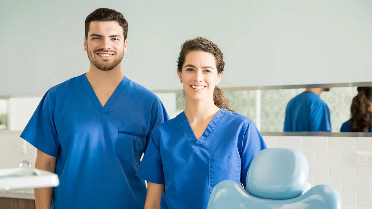 Two smiling pediatric dental assistants in blue scrubs in Georgia clinic.