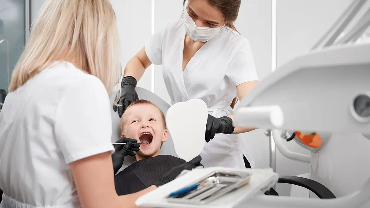 Pediatric dentist and dental assistant clearning child's teeth.