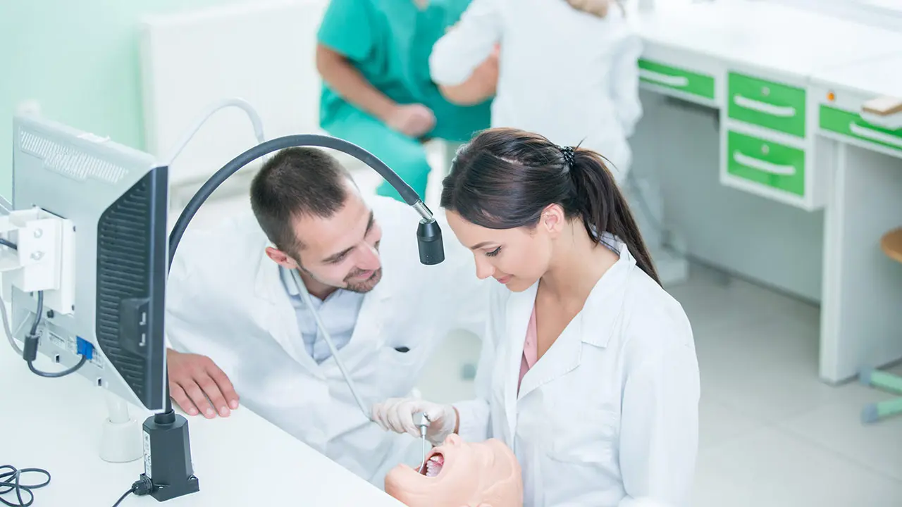 Pediatric dental school instructor showing student how to clean teeth.