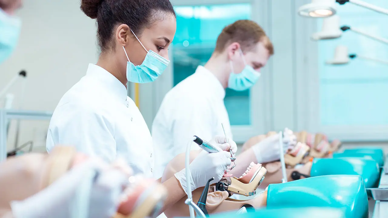 Students practicing dental procedures on training models in a classroom, learning the hands-on skills needed to become a pediatric dental assistant.